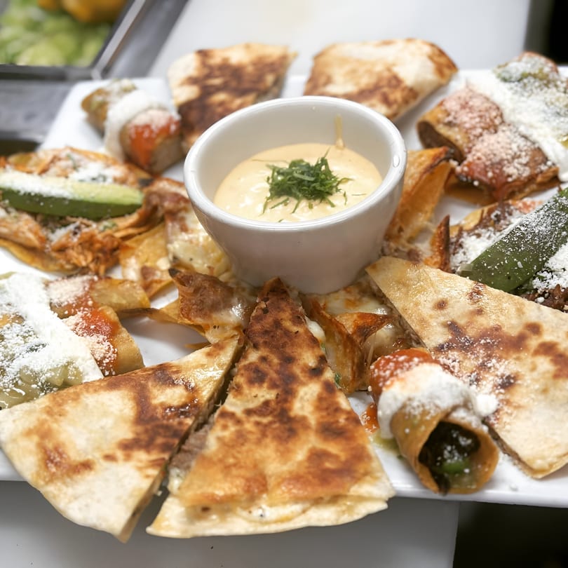 A platter of various Mexican appetizers, including quesadillas, taquitos, and a central dip.