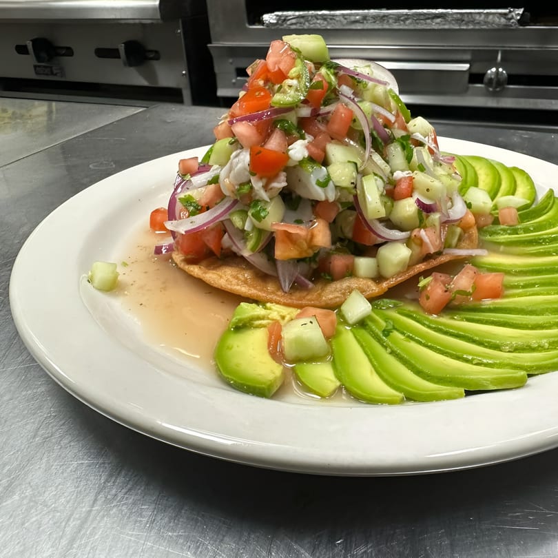 A vibrant Cinco de Mayo 2 ceviche tostada with avocado slices on a white plate.