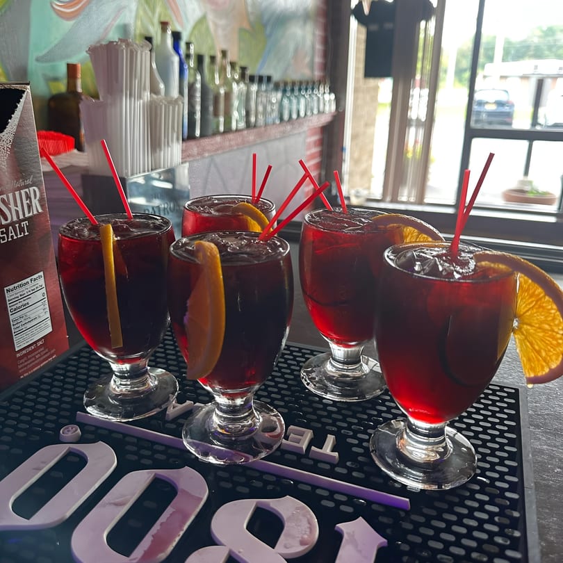 Four red sangrias with orange slices and red straws on a bar mat at Cinco de Mayo 2.