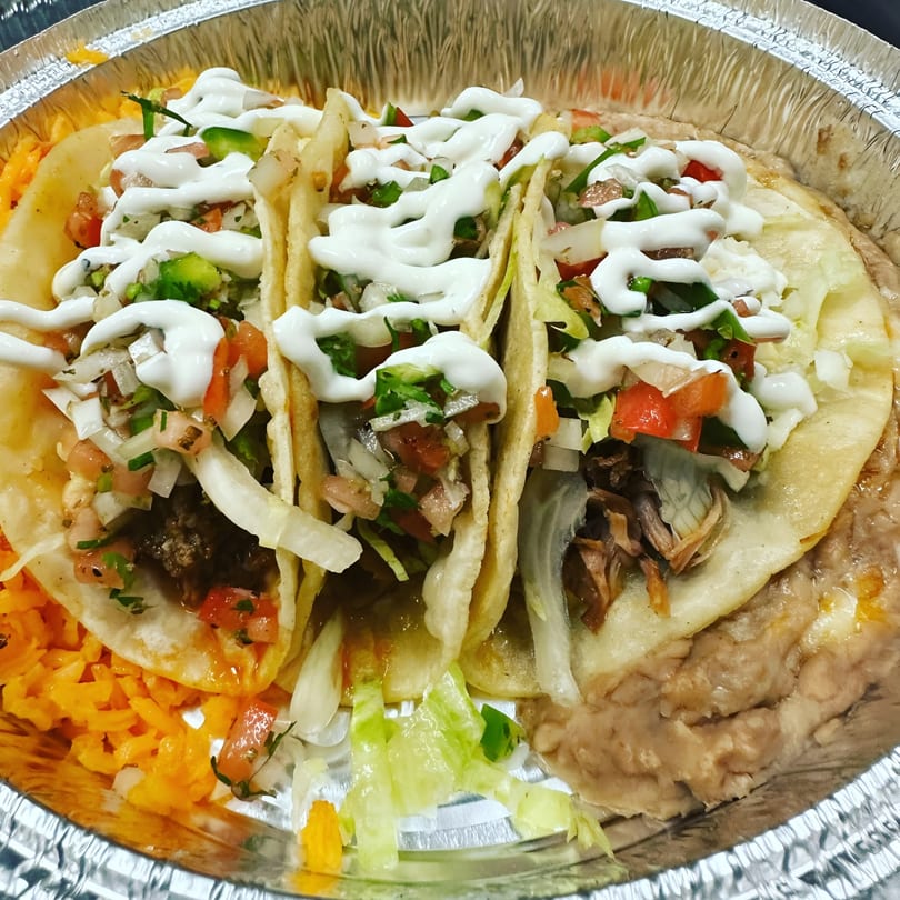 Three Cinco de Mayo 2 tacos with sour cream, pico de gallo, rice, and refried beans.