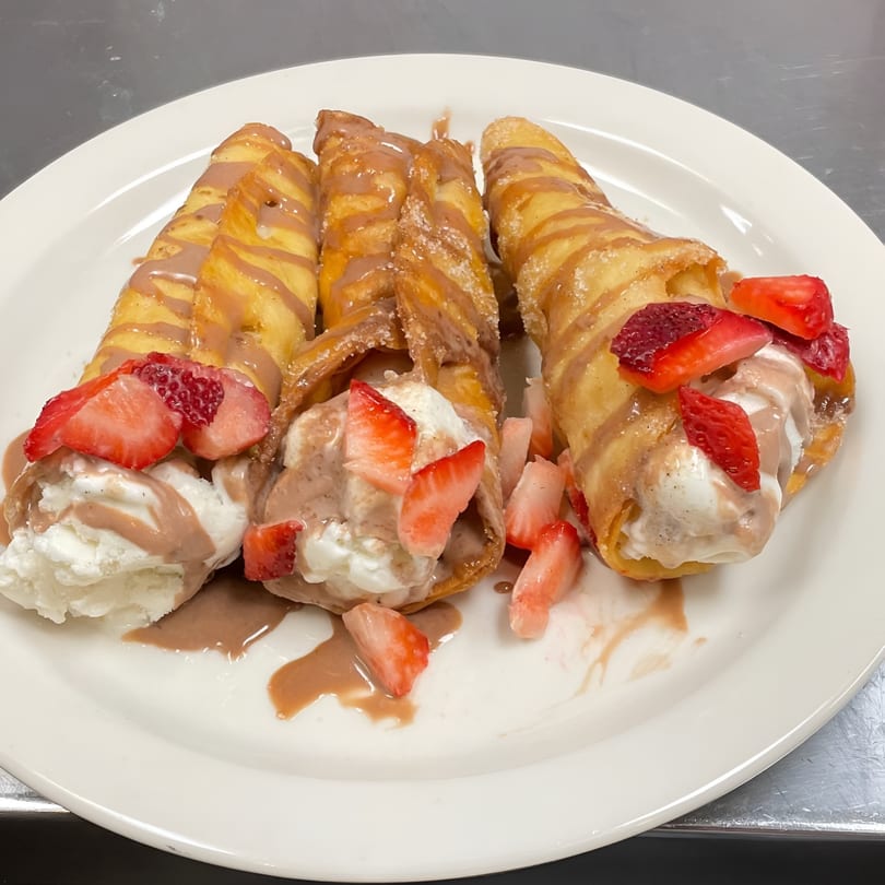 Three churros filled with ice cream, drizzled with chocolate sauce, and topped with fresh strawberries.