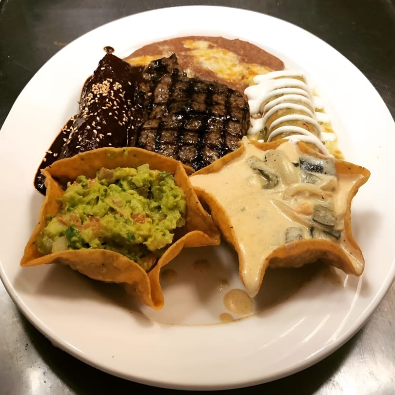 Mexican platter with grilled steak, mole, refried beans, enchilada, guacamole, and queso fundido.