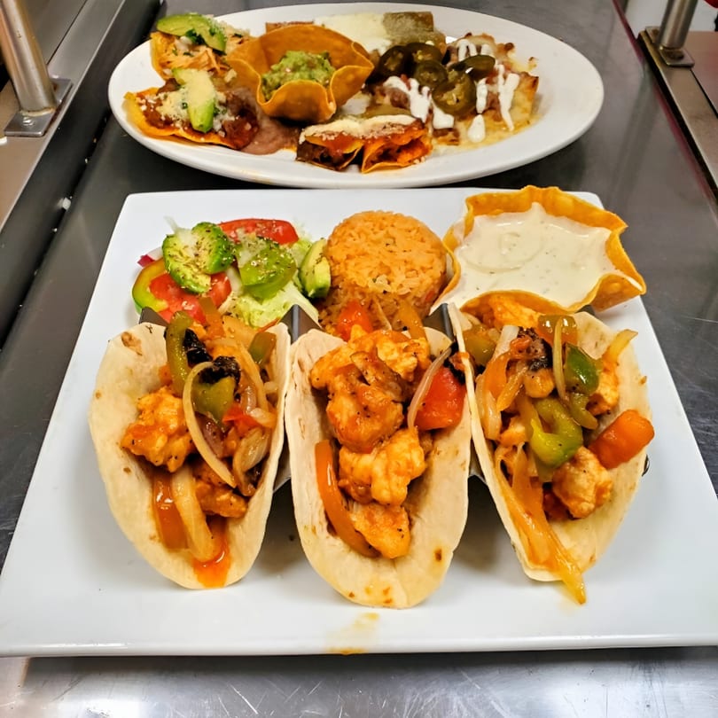 Three shrimp tacos with rice and salad, and a plate of nachos with guacamole and jalapeños.